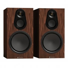 Isometric view of a pair of Monitor Audio Silver 100 8G bookshelf speakers showcasing the walnut wood veneer cabinets, exposed drivers, and gold dome tweeters.